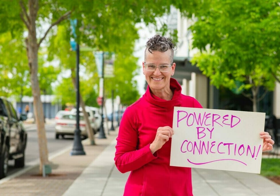 Ginger Johnson holding a sign that says "Powered By Connection"